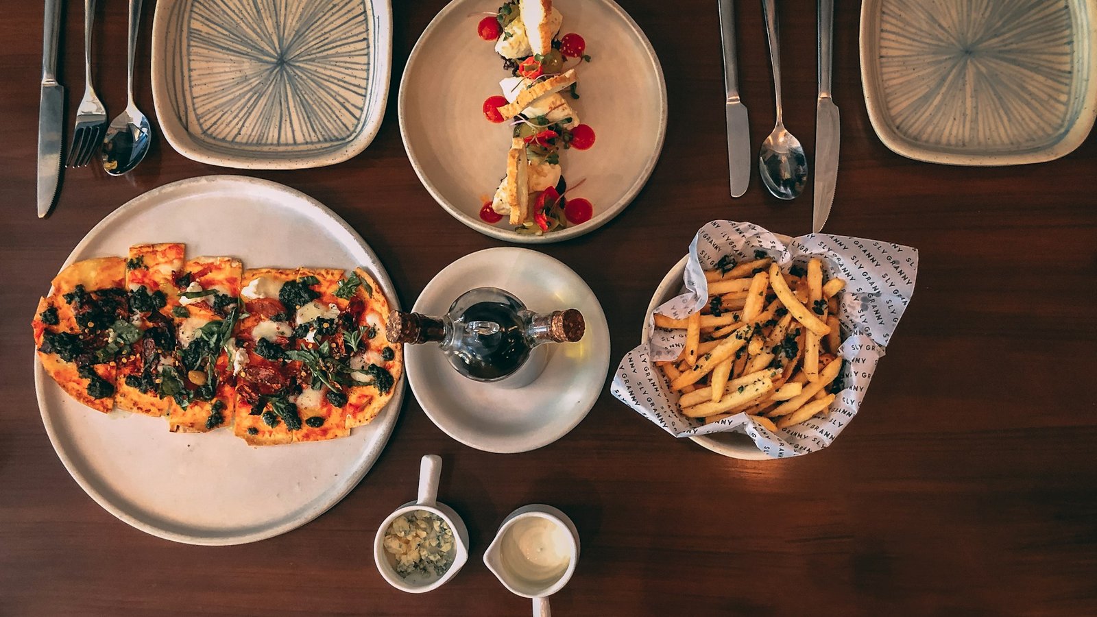 Overhead view of pizza, fries and a plated dish on a wooden restaurant table in Delhi