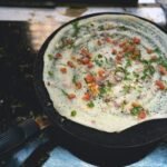 Vegetable-topped dosa cooking on a round griddle in Mumbai