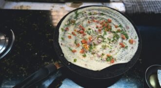 Vegetable-topped dosa cooking on a round griddle in Mumbai
