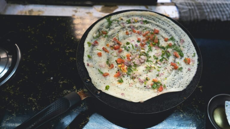 Vegetable-topped dosa cooking on a round griddle in Mumbai