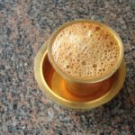 Frothy South Indian filter coffee in a metal tumbler and dabarah